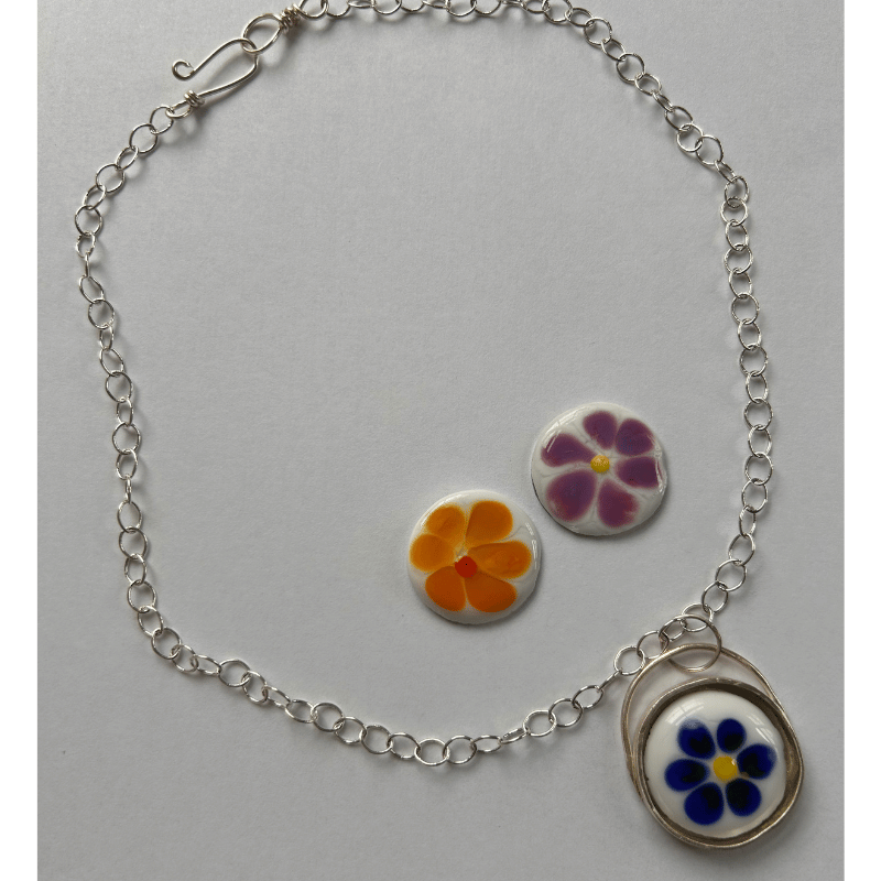 A silver chain necklace with a circular pendant featuring three ball markers in a floral pattern in blue, purple and orange.
